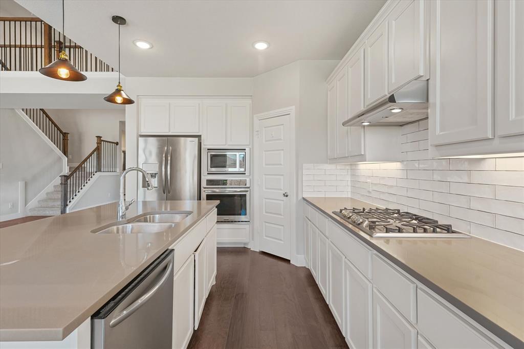 2044 Longbridge Road Forney, TX 75126 - Photo 9 of 40 Contemporary kitchen featuring white cabinetry, stainless steel appliances, a center island with double sink, subway tile backsplash, and dark wood-finish flooring