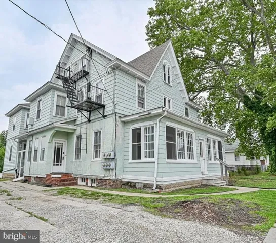 a view of a white house next to a yard with big trees