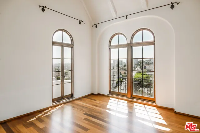 an empty room with wooden floor and way to kitchen