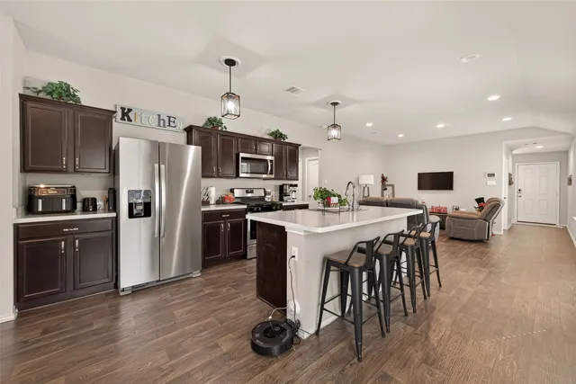a kitchen with stainless steel appliances kitchen island granite countertop a refrigerator a stove a sink a dining table and chairs with wooden floor