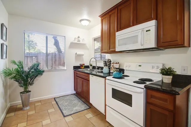 a kitchen with stainless steel appliances granite countertop white cabinets a stove a sink and a potted plant