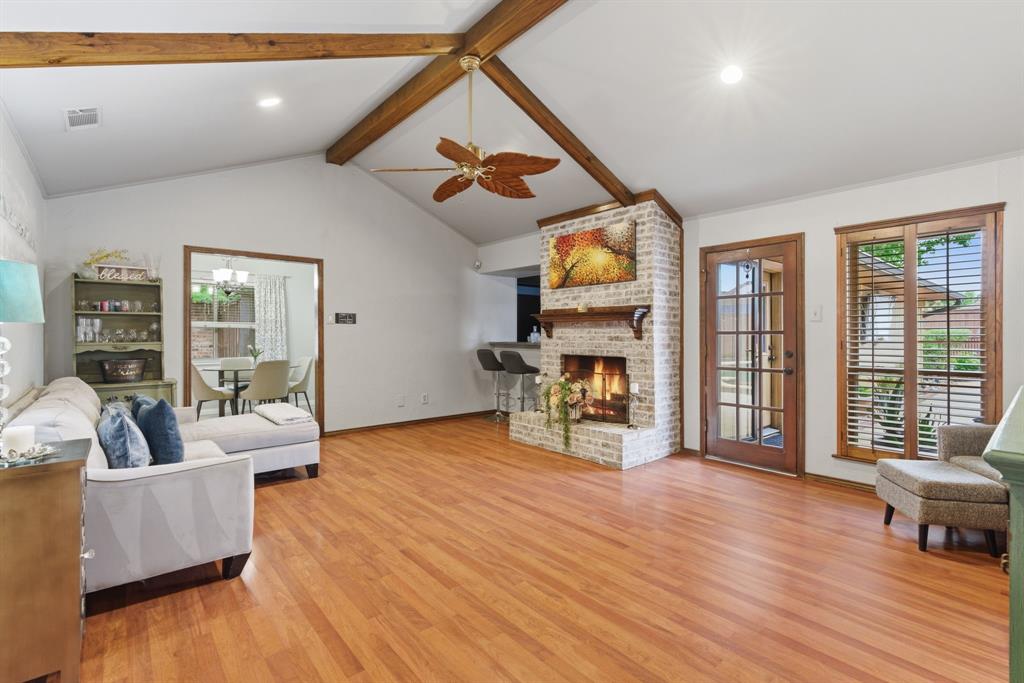 2307 Castle Rock Road Carrollton, TX 75007 - Photo 6 of 34 Spacious living area featuring hardwood flooring, a vaulted ceiling with exposed wooden beams, and a brick fireplace