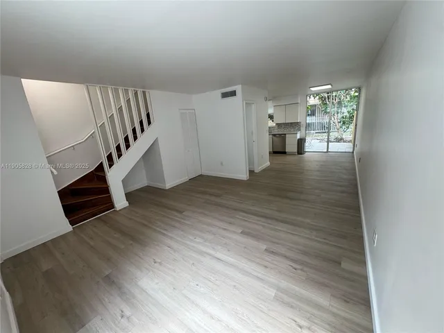 a view of an empty room with wooden floor and stairs