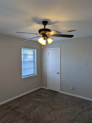 an empty room with a chandelier fan and windows