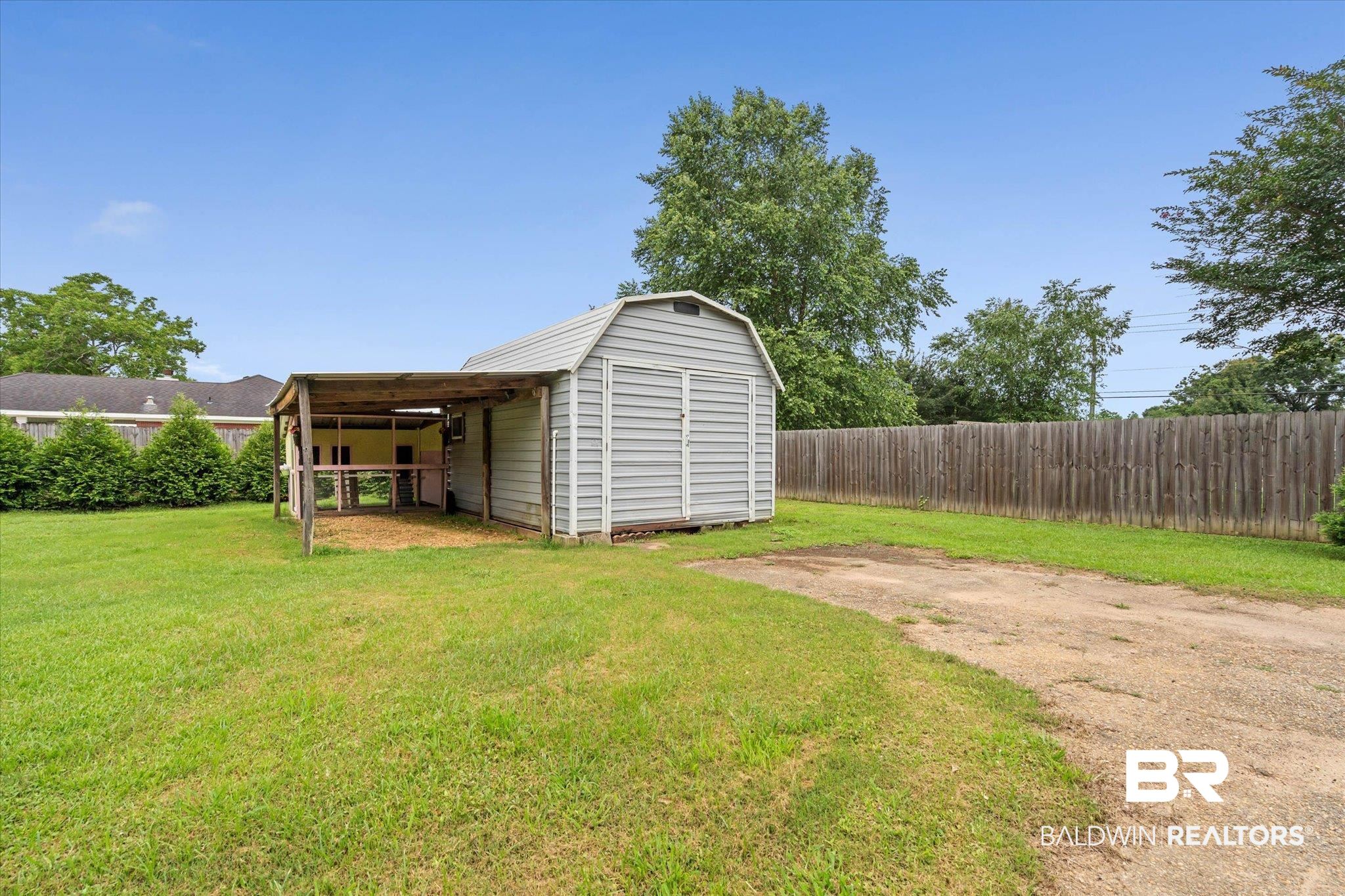 3170 Scott Dairy Loop Road West Mobile, AL 36695 - Photo 20 of 24 Detached storage shed with an attached covered lean-to structure, set on a grassy yard with a wooden privacy fence