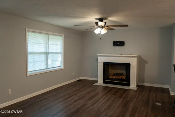 a view of an empty room with wooden floor fireplace and a window