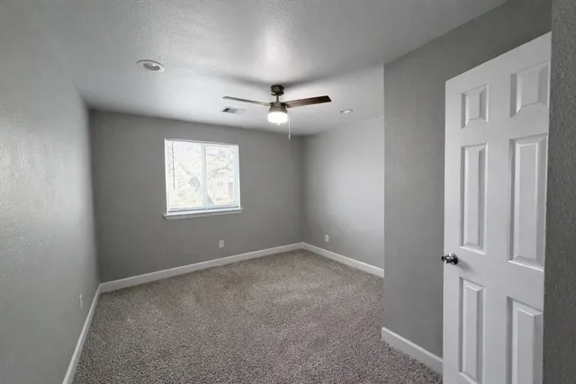 an empty room with ceiling fan and windows