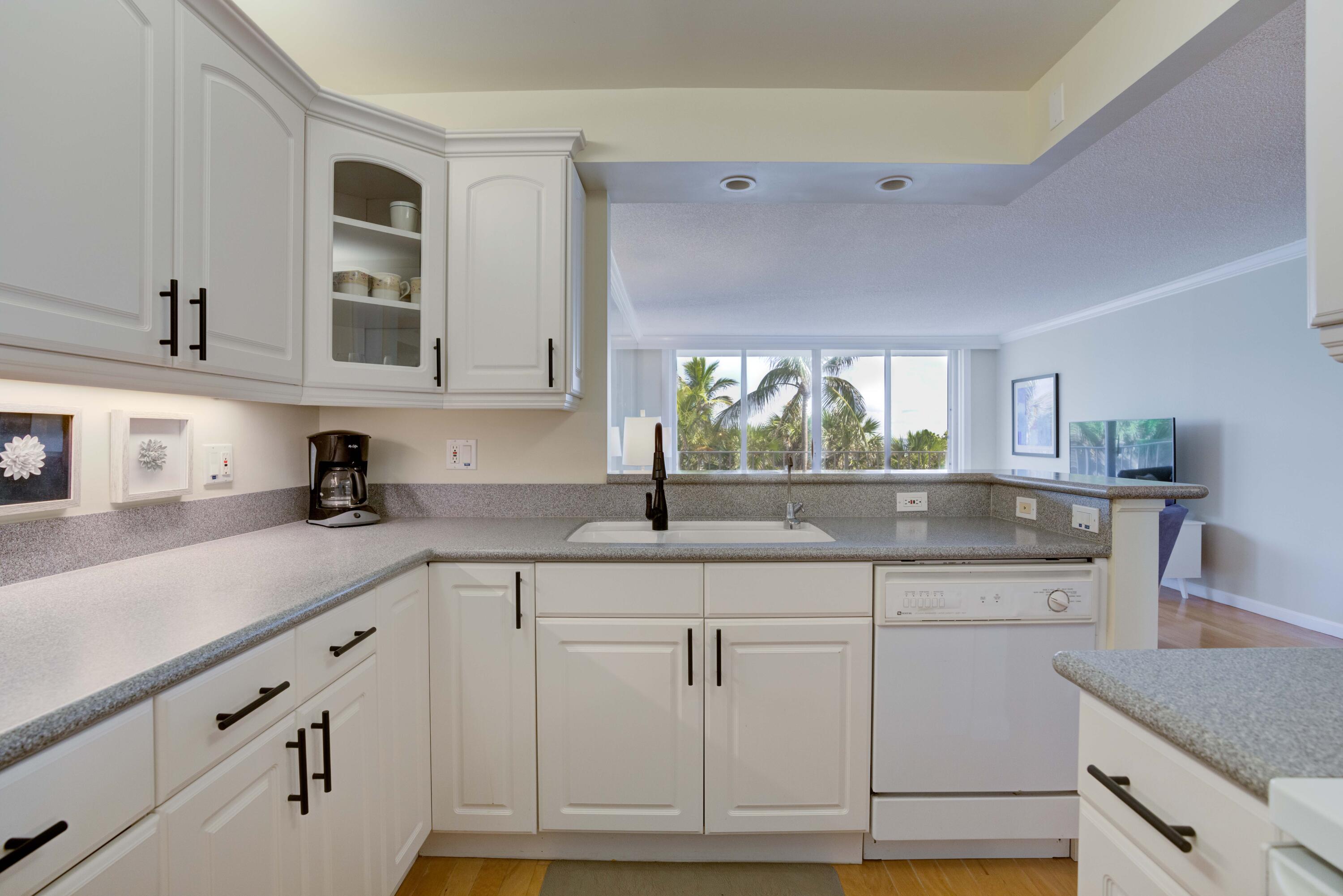 630 Ocean Drive, Unit 302 Juno Beach, FL 33408 - Photo 9 of 40 a kitchen with granite countertop white cabinets and white appliances