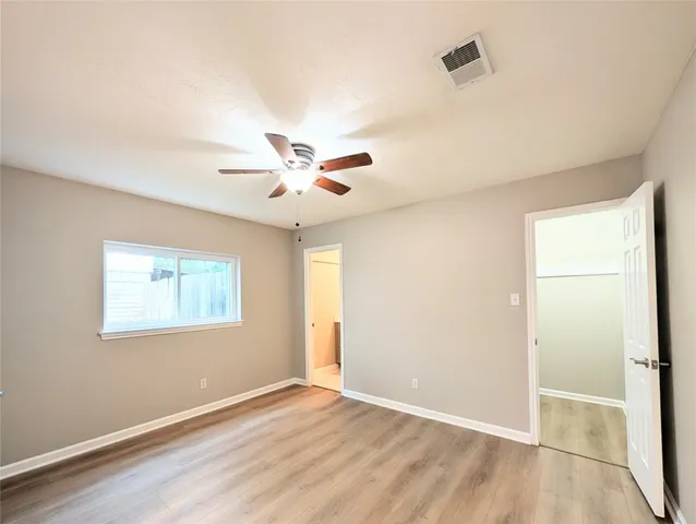 an empty room with wooden floor fan and windows