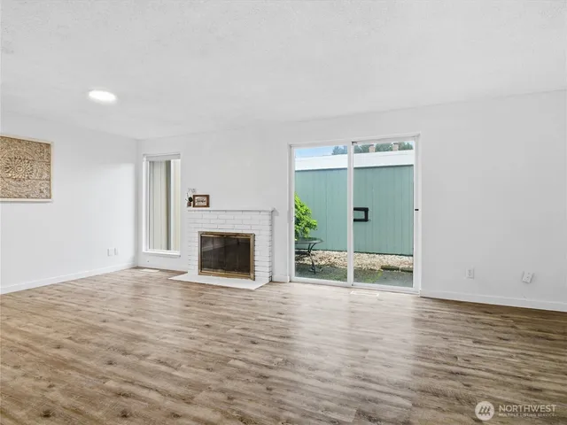 a view of an empty room with wooden floor fireplace and a window