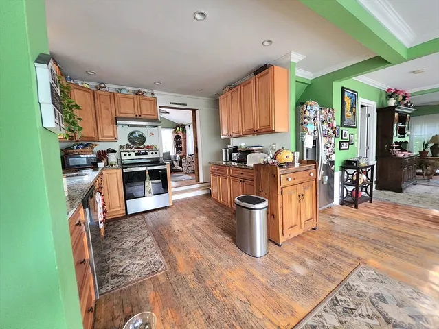 a kitchen with stainless steel appliances granite countertop a stove top oven a sink dishwasher a dining table and chairs with wooden floor