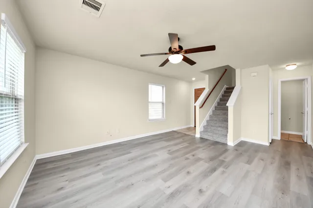 an empty room with wooden floor fan and windows