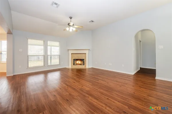 an empty room with wooden floor chandelier fan and windows