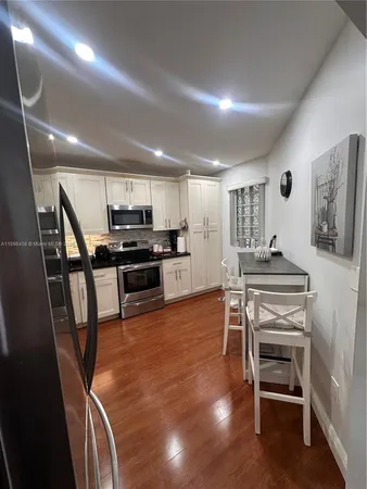 a kitchen with stainless steel appliances kitchen island granite countertop a stove top oven a sink a dining table and chairs with wooden floor