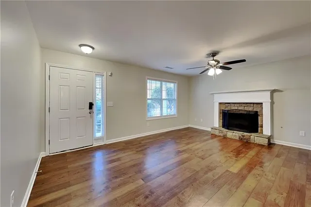 a view of an empty room with wooden floor fireplace and a window