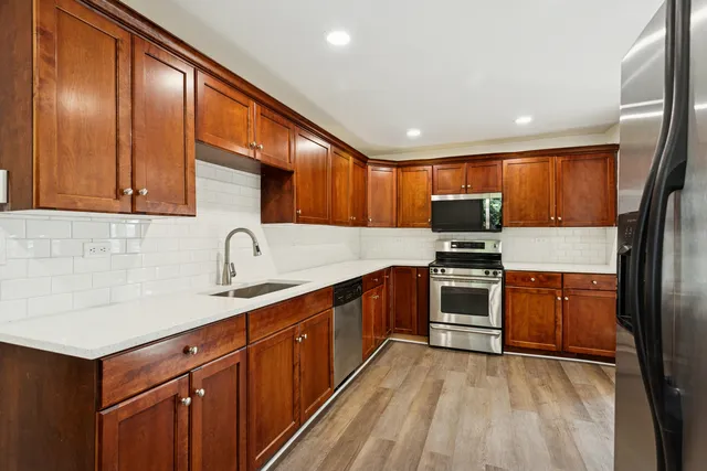 a kitchen with stainless steel appliances granite countertop wooden cabinets a sink dishwasher a stove and a refrigerator with wooden floor