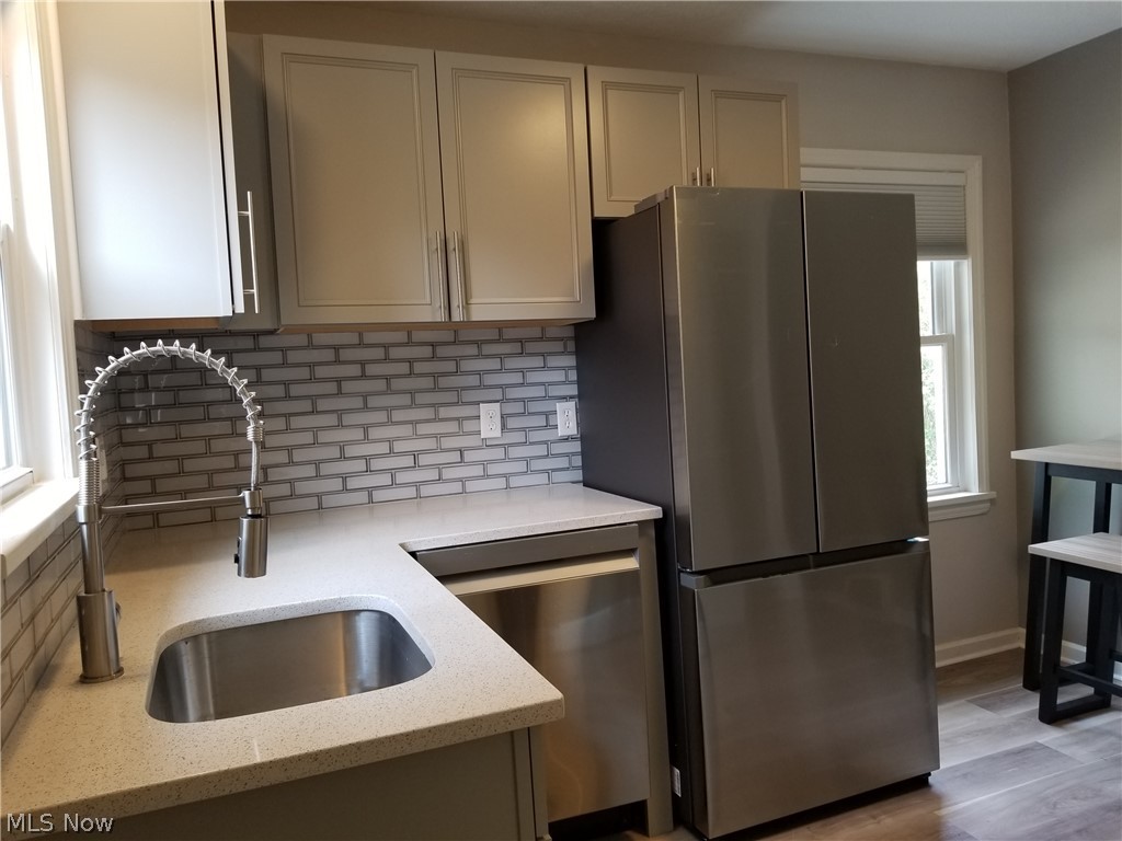 5671 Wellington Road Cleveland, OH 44124 - Photo 5 of 26 Kitchen featuring stainless steel appliances, light hardwood / wood-style floors, light stone countertops, decorative backsplash, and sink