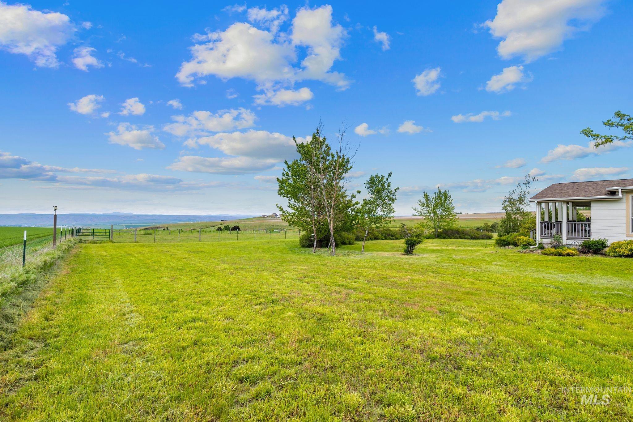 37989 Rosenkrantz Road Lewiston, ID 83501 - Photo 48 of 50 Expansive grassy property featuring a partial white-sided residence with a covered porch, mature and young trees, a distant landscape, and a partial fence line