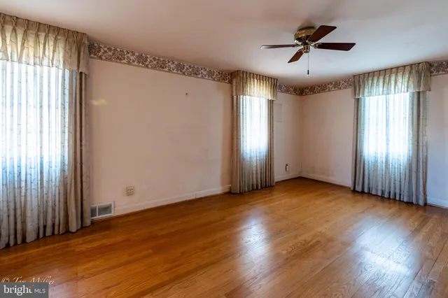 an empty room with wooden floor fan and windows