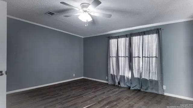 an empty room with wooden floor fan and windows