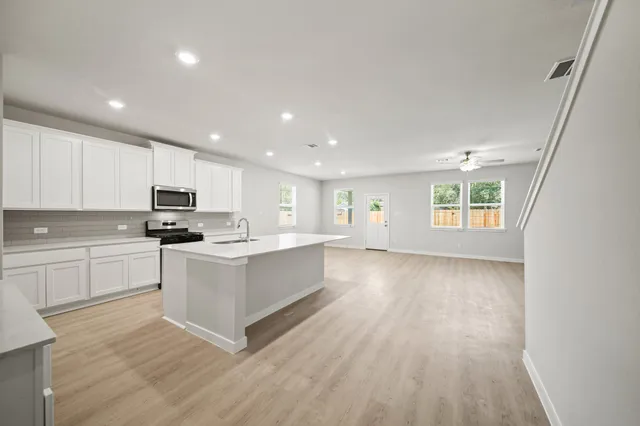 a kitchen with stainless steel appliances granite countertop a stove top oven a sink dishwasher and a refrigerator with wooden floor