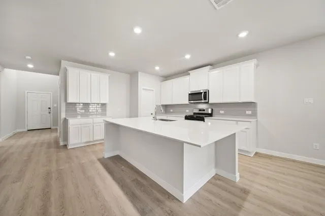 a kitchen with stainless steel appliances granite countertop a stove top oven a sink dishwasher and a refrigerator with wooden floor