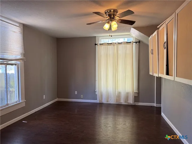 an empty room with wooden floor and windows with curtains
