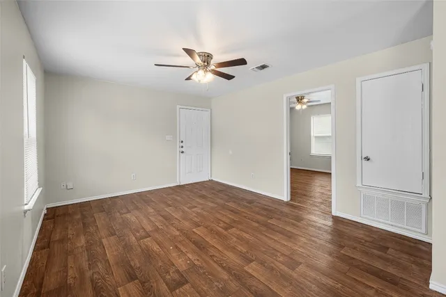 an empty room with wooden floor ceiling fan and windows