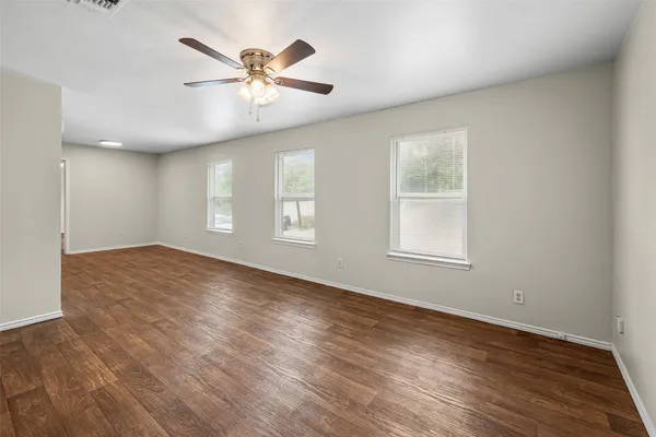 an empty room with wooden floor fan and windows
