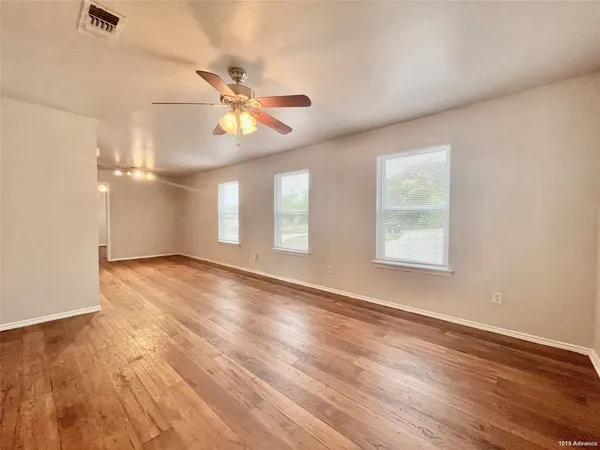 an empty room with wooden floor ceiling fan and windows