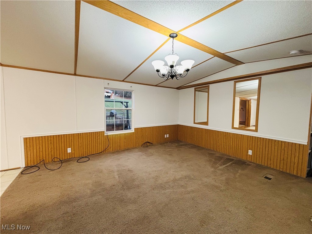 202 Pullman Road Pennsboro, WV 26415 - Photo 6 of 23 Empty room with wood walls, lofted ceiling, carpet flooring, a textured ceiling, and a chandelier