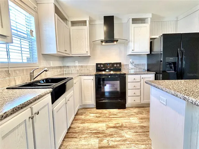 a kitchen with stainless steel appliances granite countertop a stove top oven a refrigerator a sink and dishwasher with wooden floor