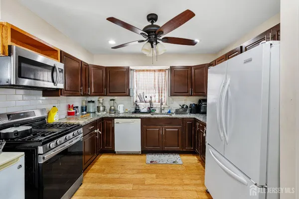 a kitchen with stainless steel appliances granite countertop a stove top oven a refrigerator a sink and dishwasher with wooden floor