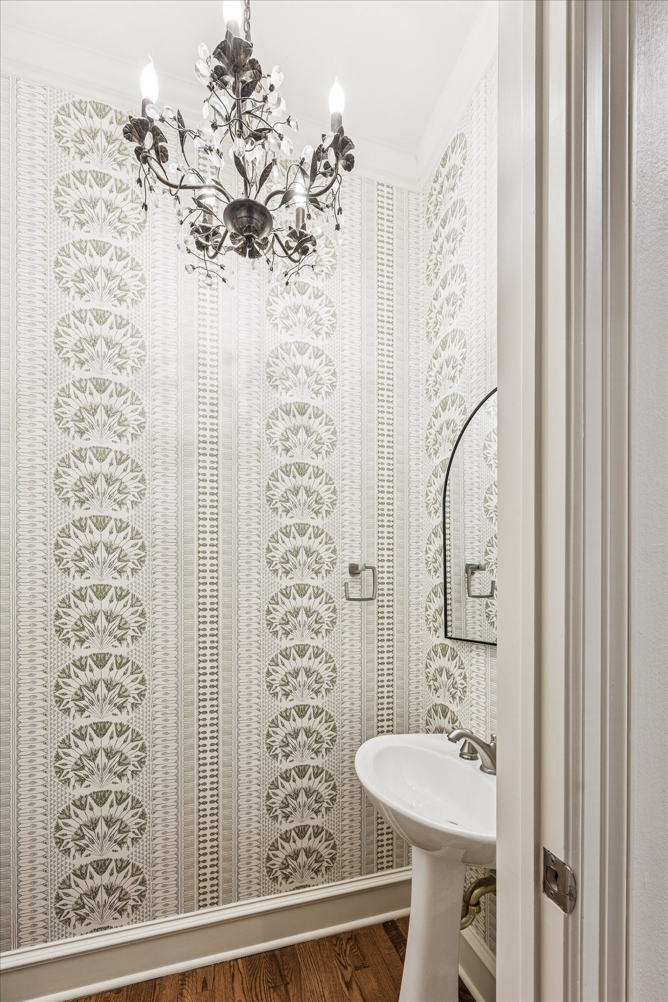 5823 Augusta Court Houston, TX 77057 - Photo 19 of 44 A stylish powder room featuring elegant patterned wallpaper, a classic pedestal sink, and a decorative chandelier. The space is enhanced by warm wood flooring, adding a touch of sophistication.