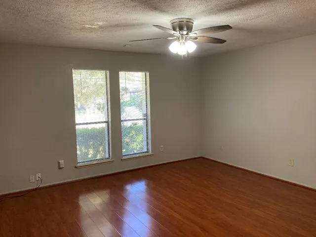 an empty room with wooden floor chandelier fan and windows
