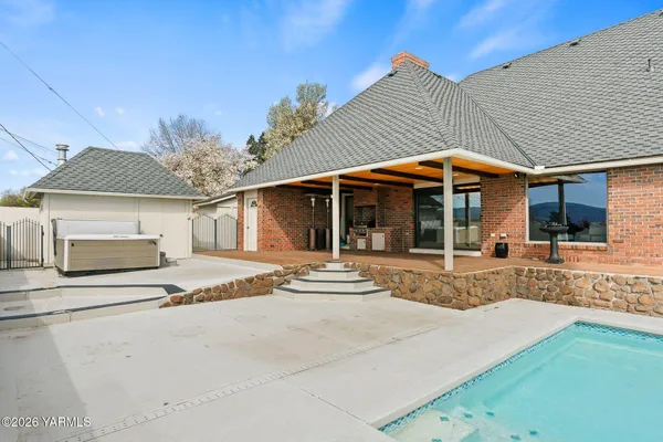 a view of a white house with a swimming pool table and chairs under an umbrella