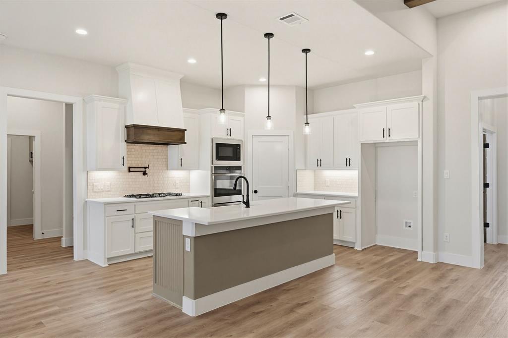 6713 Odom Road Sanger, TX 76266 - Photo 10 of 32 a kitchen with stainless steel appliances kitchen island granite countertop a sink a stove a refrigerator and white cabinets with wooden floor