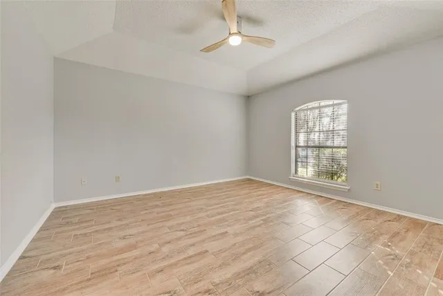 a view of an empty room with wooden floor and a ceiling fan