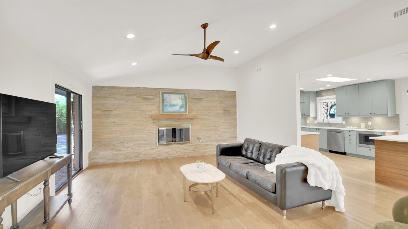 7510 Daugherty Street Austin, TX 78757 - Photo 12 of 37 Living room featuring vaulted ceiling, light wood finished floors, a glass covered fireplace, a ceiling fan, and recessed lighting