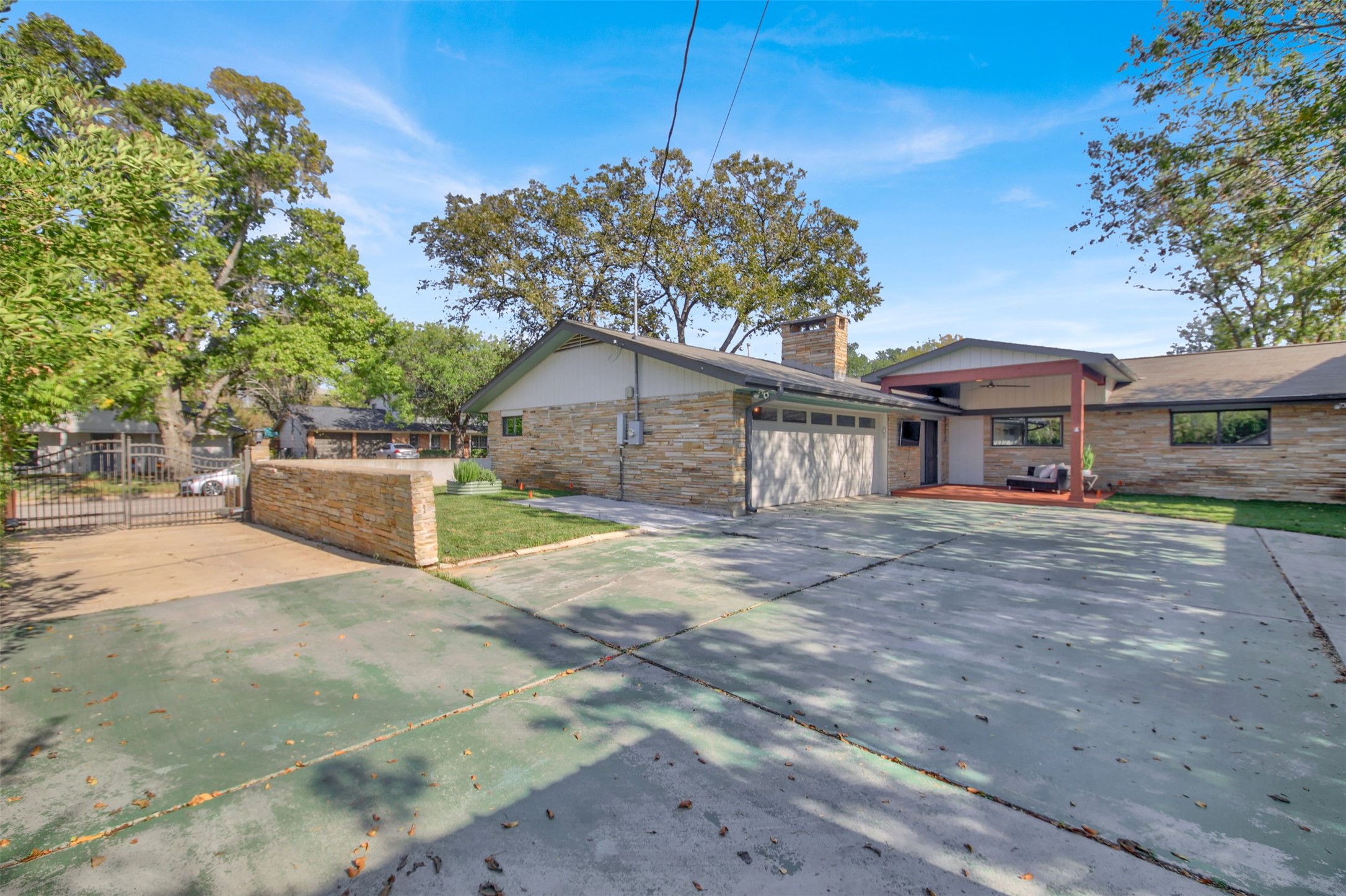 7510 Daugherty Street Austin, TX 78757 - Photo 22 of 37 View of property exterior featuring a chimney, driveway, a garage, a gate, and stone siding