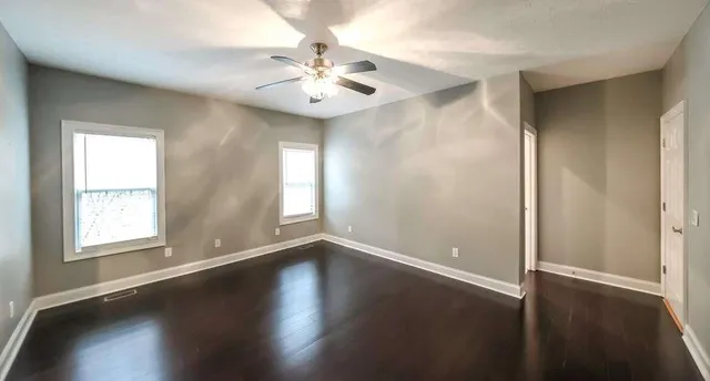 an empty room with wooden floor fan and windows