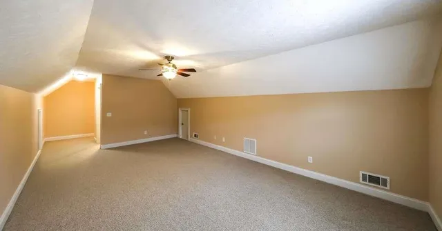 an empty room with chandelier fan and windows