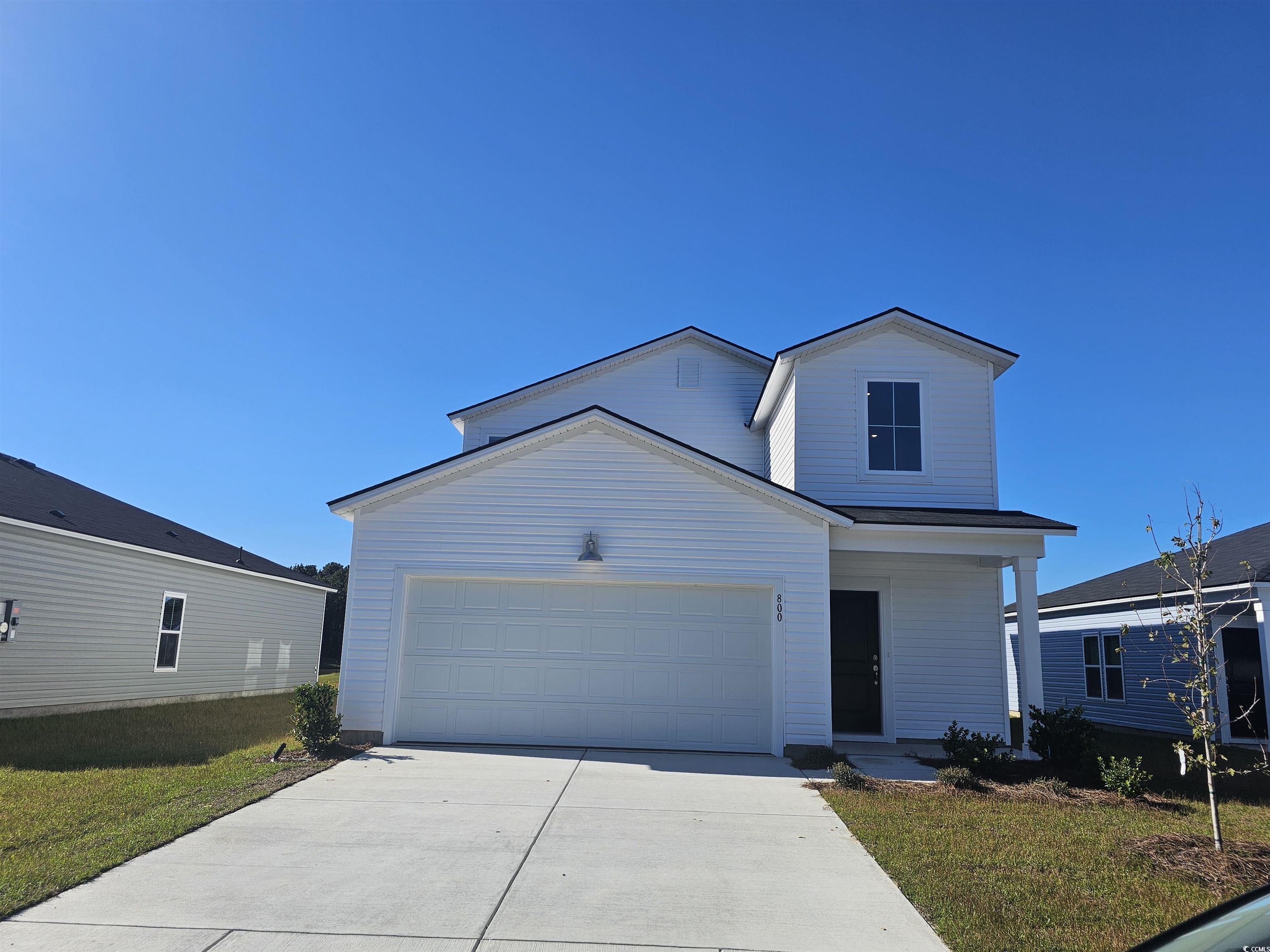 Traditional-style house featuring concrete driveway, a front yard, an attached garage, and a porch