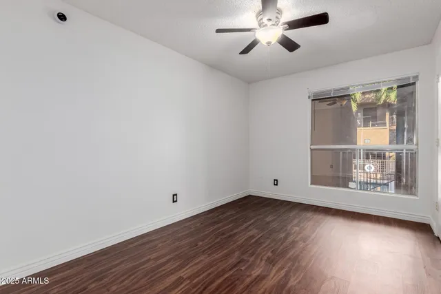 an empty room with wooden floor chandelier fan and windows