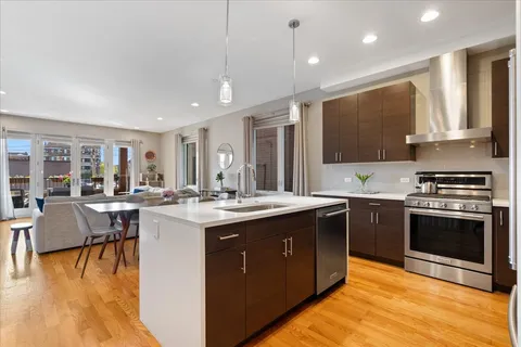 a kitchen with stainless steel appliances granite countertop a stove top oven a sink dishwasher a dining table and chairs with wooden floor