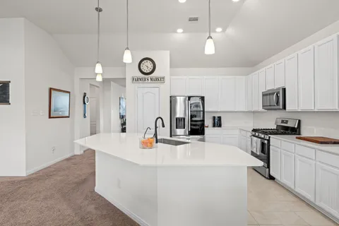a kitchen with stainless steel appliances a stove a sink a microwave a refrigerator cabinets and living room view
