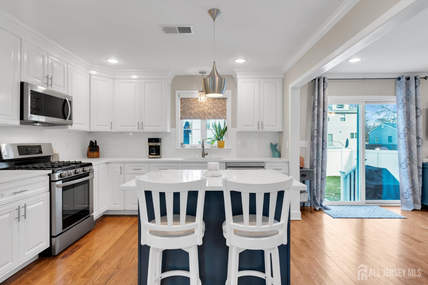 3 Harrison Avenue Aberdeen, NJ 07747 - Photo 14 of 46 a kitchen with stainless steel appliances granite countertop a stove a sink a microwave a refrigerator white cabinets and chairs with wooden floor
