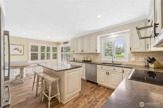 a kitchen with stainless steel appliances granite countertop a stove top oven a sink a dining table and chairs with wooden floor