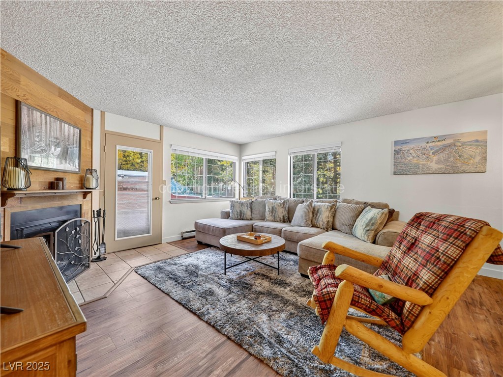 Living room with a fireplace with flush hearth, a textured ceiling, wood finished floors, and a baseboard heating unit