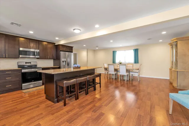 a kitchen with stainless steel appliances granite countertop a stove top oven a sink dishwasher a dining table and chairs with wooden floor